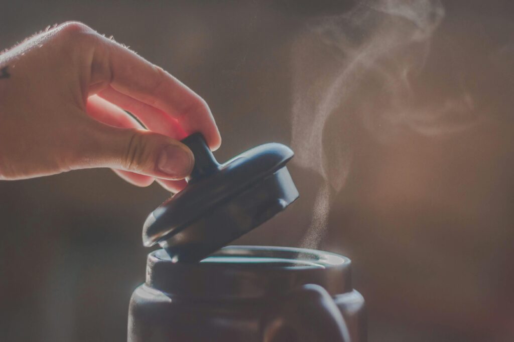 Close-up of a hand lifting a pot lid, revealing steam rising inside.